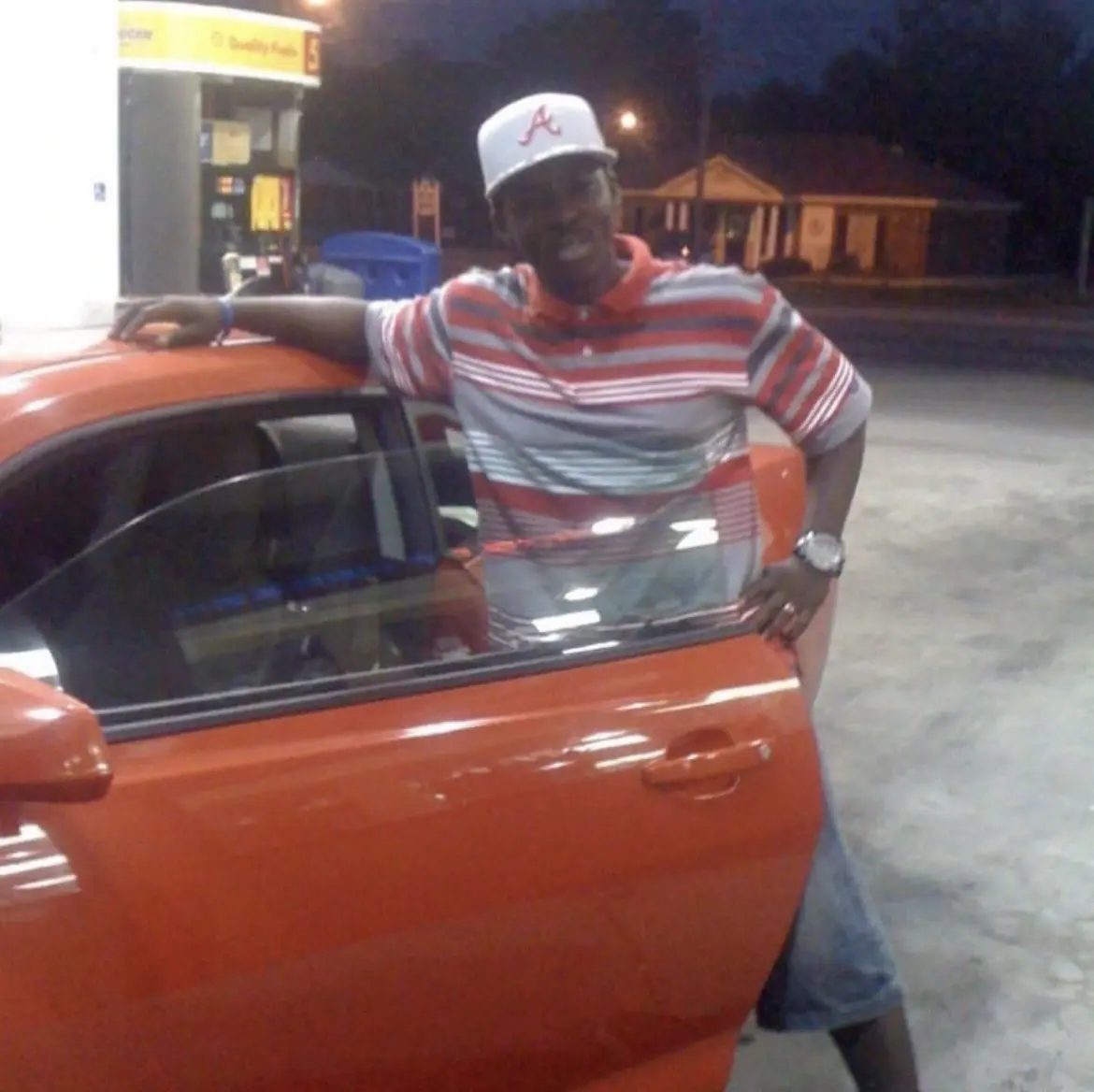 The Author J.K. Wade, hopping out of a Orange Camaro, wearing a orange gray and white striped shirt.