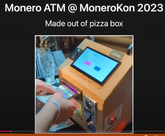 Monero ATM at MoneroKon 2023 made out of pizza box display and raspbery pi the person inserting paper money to working Monero ATM