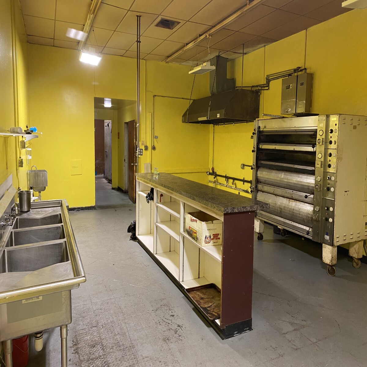 a commercial kitchen with a pizza oven, hood, and sink