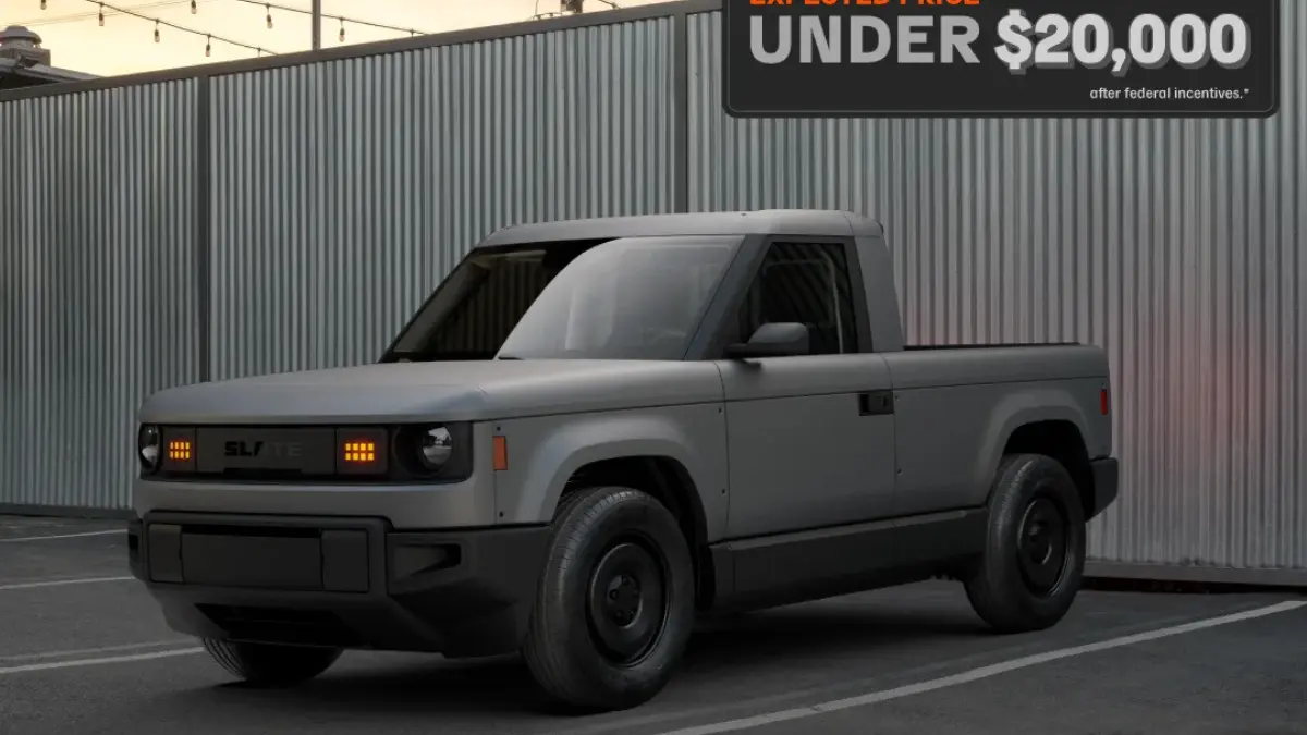 Slate Truck parked in front of a corrugated steel wall, showcasing its minimalist, rugged design with a starting price under $20,000.