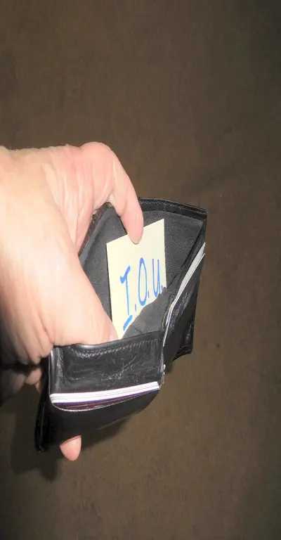 A hand holding open an otherwise empty wallet with a paper that reads