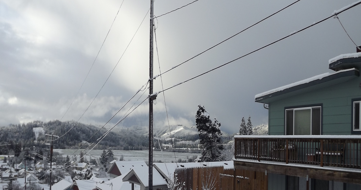 A small town with snow-covered roofs, set against snowy mountains covered in pine trees.