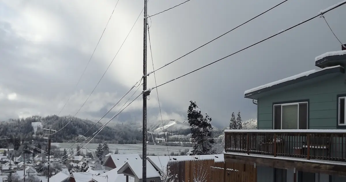 A small town with snow-covered roofs, set against snowy mountains covered in pine trees.
