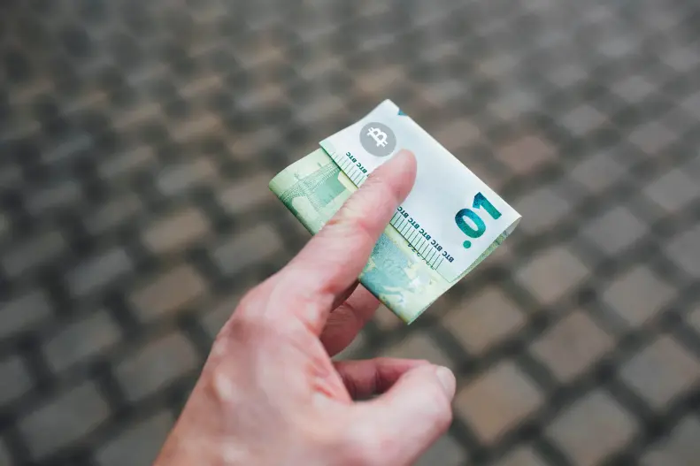 A hand holding a BTC .01 physical bill