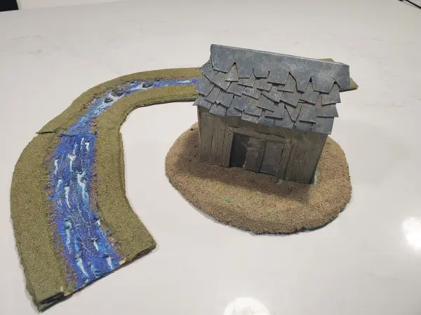A miniature house made with cardboard is shown with the modular river.