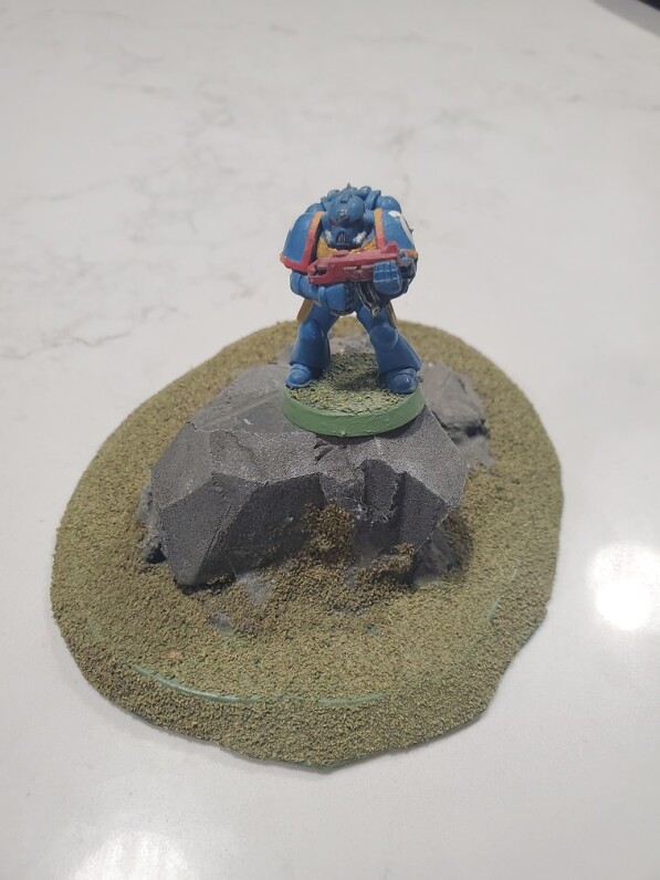 A Space Marine (WH40k) is positioned on top of the rock