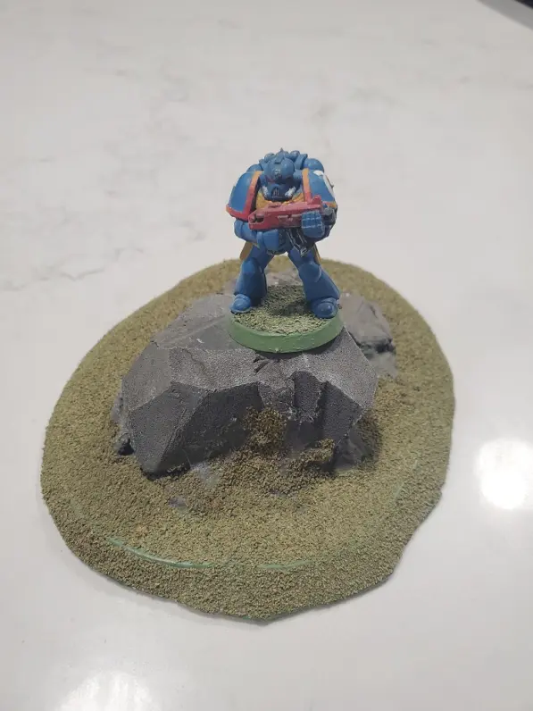 A Space Marine (WH40k) is positioned on top of the rock